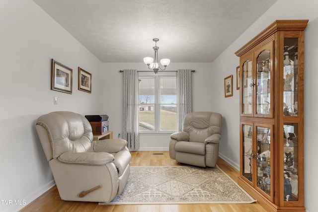 sitting room with baseboards, an inviting chandelier, and light wood finished floors