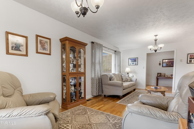 living room with a textured ceiling, baseboards, a notable chandelier, and light wood finished floors