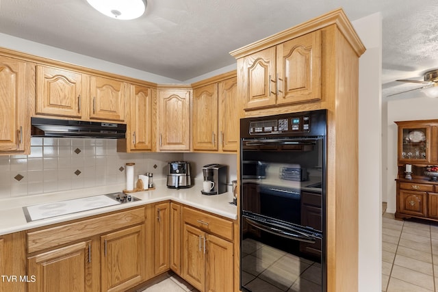 kitchen featuring dobule oven black, under cabinet range hood, white electric cooktop, light tile patterned flooring, and decorative backsplash