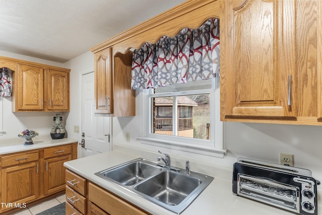 kitchen featuring a toaster, a sink, light countertops, a textured ceiling, and brown cabinets