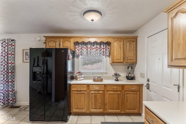 kitchen featuring brown cabinetry, a textured ceiling, black fridge, and light countertops