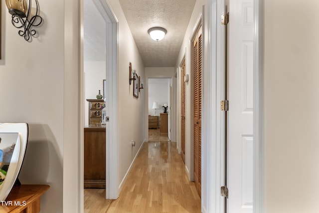 hall featuring a textured ceiling, light wood-type flooring, and baseboards