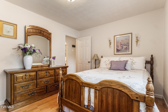 bedroom featuring baseboards, light wood-type flooring, and a textured ceiling