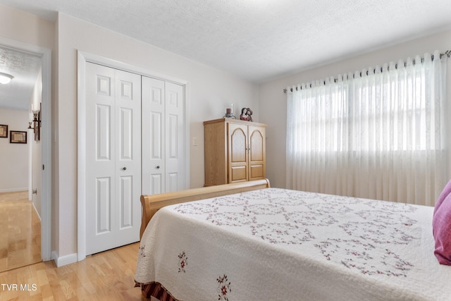 bedroom featuring a closet, a textured ceiling, light wood-type flooring, and baseboards