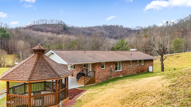 back of property featuring a gazebo, a lawn, a wooded view, and a chimney