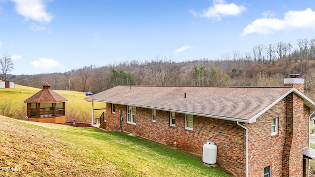 back of property with brick siding, roof with shingles, a gazebo, a lawn, and a chimney