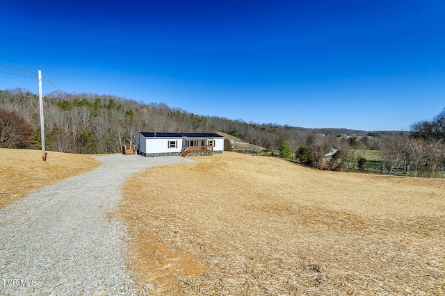 view of front facade featuring gravel driveway and a wooded view