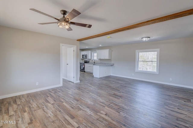 unfurnished living room with ceiling fan, a sink, baseboards, and wood finished floors