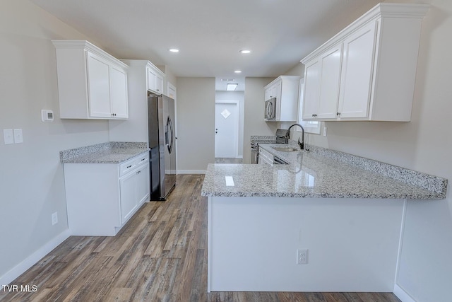 kitchen with a sink, wood finished floors, white cabinets, appliances with stainless steel finishes, and light stone countertops