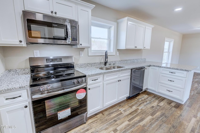 kitchen with white cabinets, a peninsula, stainless steel appliances, light wood-type flooring, and a sink