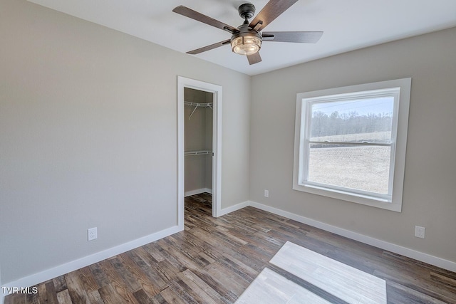 unfurnished bedroom with a closet, wood finished floors, a walk in closet, and baseboards