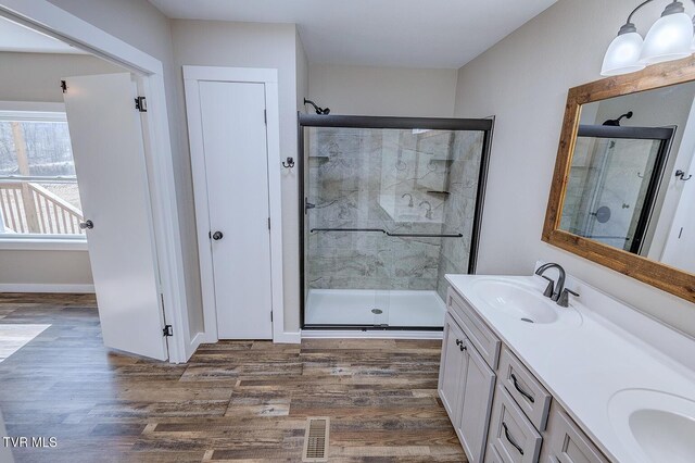 full bathroom with wood finished floors, a sink, visible vents, a shower stall, and double vanity