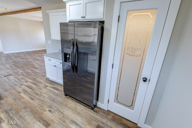 kitchen with light wood-style flooring, fridge with ice dispenser, white cabinetry, and light stone counters