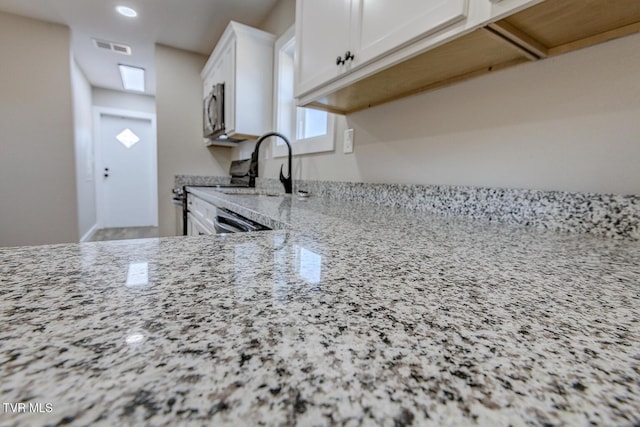 kitchen with stainless steel appliances, a sink, visible vents, white cabinets, and light stone countertops