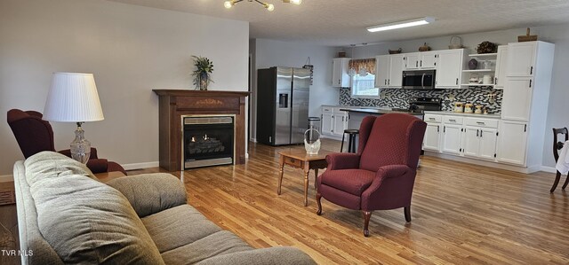 living room featuring light wood finished floors, a fireplace, baseboards, and a textured ceiling