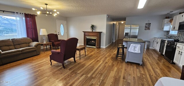 living room with a textured ceiling, a chandelier, baseboards, a lit fireplace, and dark wood-style floors