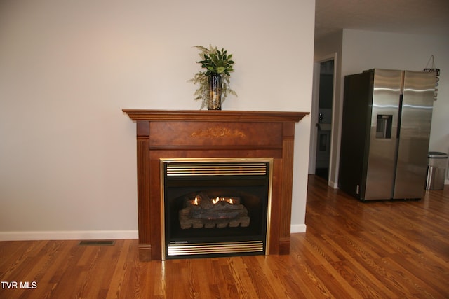 room details featuring a warm lit fireplace, stainless steel fridge, visible vents, and wood finished floors