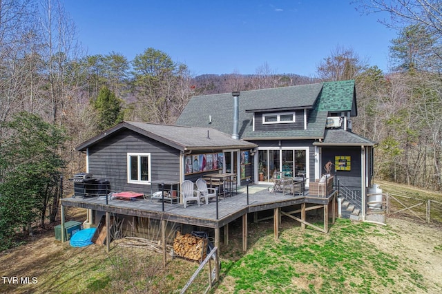 rear view of property with fence, a deck, a wooded view, and roof with shingles