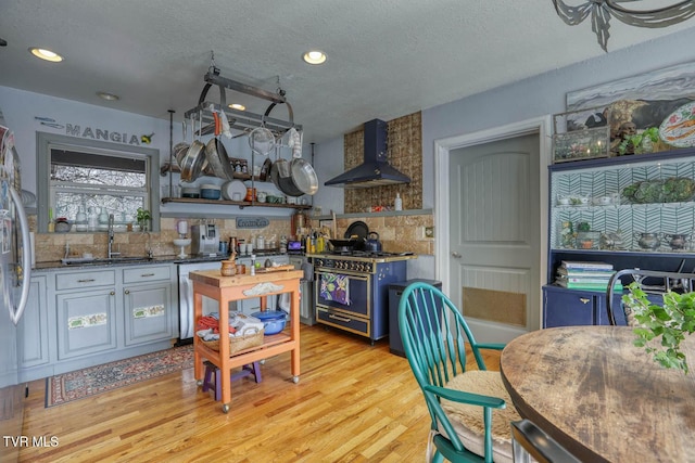 kitchen featuring stainless steel appliances, a sink, decorative backsplash, wall chimney exhaust hood, and light wood finished floors