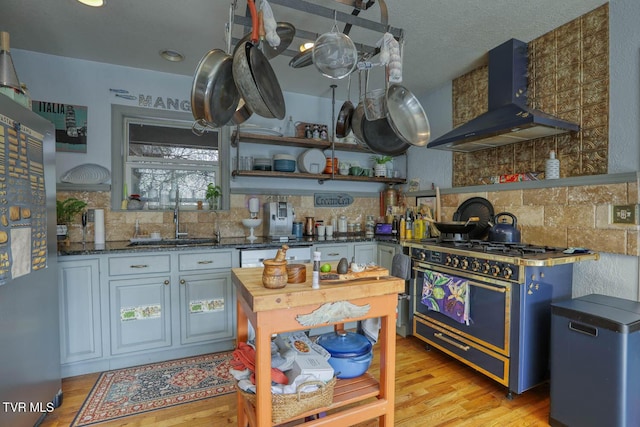 kitchen with light wood-style flooring, decorative backsplash, gas stove, a sink, and wall chimney exhaust hood