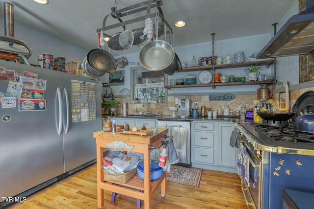 kitchen featuring stainless steel appliances, a sink, exhaust hood, light wood-style floors, and open shelves