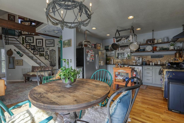 dining area featuring stairway, wet bar, a textured ceiling, light wood-style floors, and a chandelier