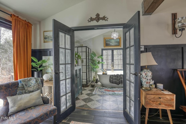 interior space with wainscoting, vaulted ceiling, dark wood-style flooring, and french doors