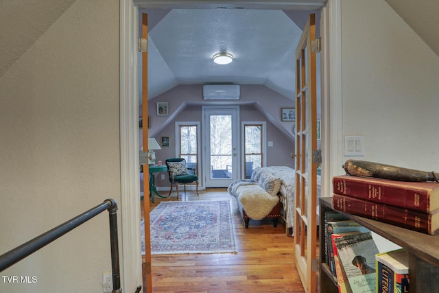 bonus room with lofted ceiling, a textured wall, a textured ceiling, wood finished floors, and a wall mounted air conditioner