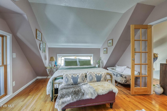 bedroom with vaulted ceiling, a textured ceiling, baseboards, and wood finished floors