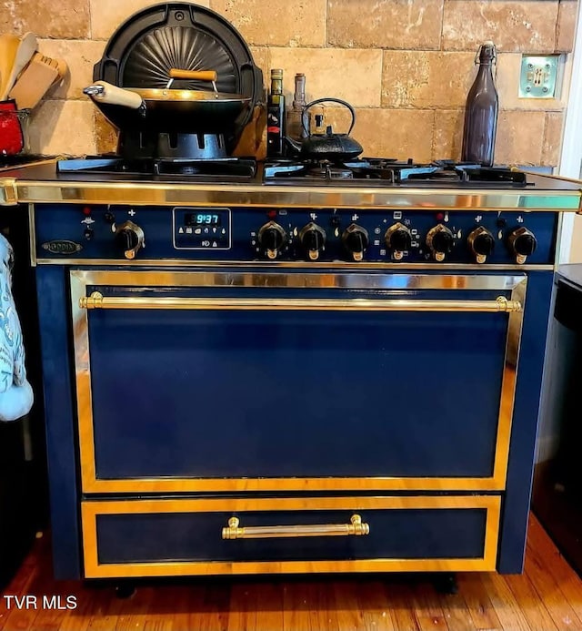 details with wood finished floors, backsplash, and gas range oven