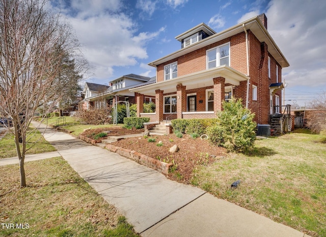 traditional style home featuring a front yard, cooling unit, covered porch, a chimney, and brick siding