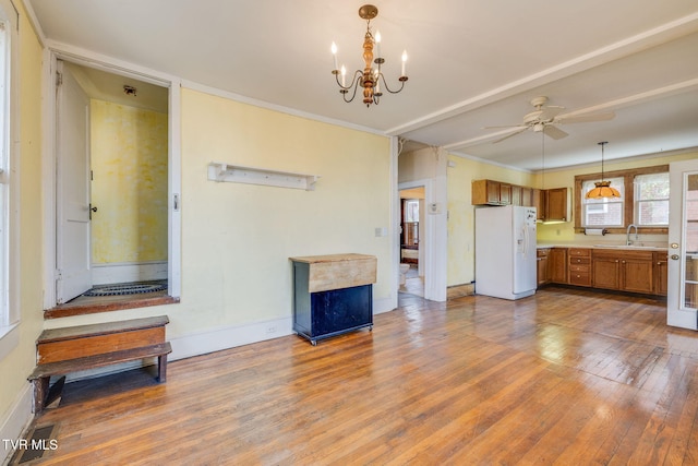 unfurnished living room featuring crown molding, baseboards, ceiling fan with notable chandelier, hardwood / wood-style flooring, and a sink