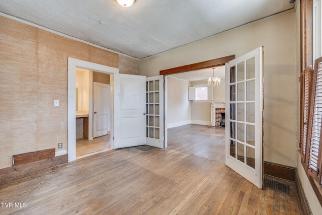 unfurnished room featuring visible vents, a brick fireplace, hardwood / wood-style floors, french doors, and an inviting chandelier