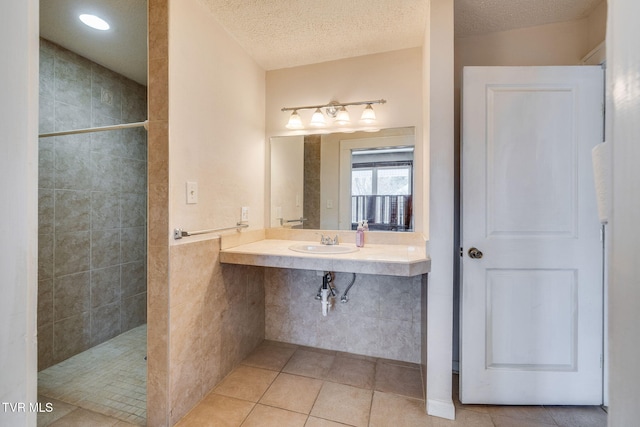 full bathroom with a sink, a textured ceiling, tile patterned floors, and a walk in shower