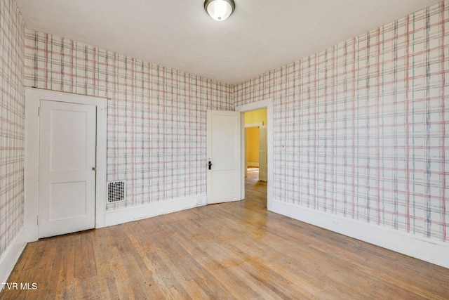 spare room featuring wallpapered walls, wood finished floors, and baseboards