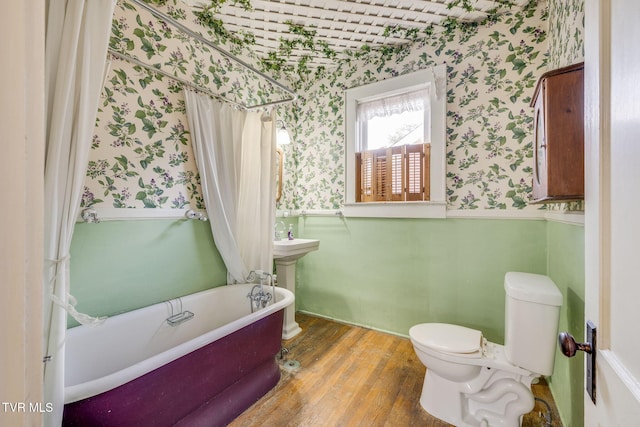 full bathroom with wallpapered walls, a freestanding bath, toilet, wainscoting, and wood finished floors