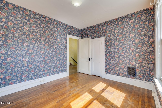 spare room with wallpapered walls, baseboards, and wood finished floors