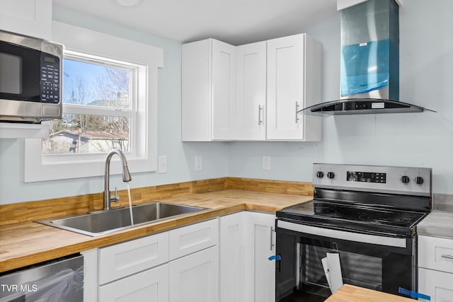 kitchen with a sink, wood counters, white cabinets, appliances with stainless steel finishes, and wall chimney exhaust hood