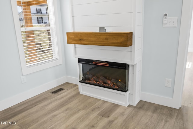 room details featuring a glass covered fireplace, visible vents, baseboards, and wood finished floors