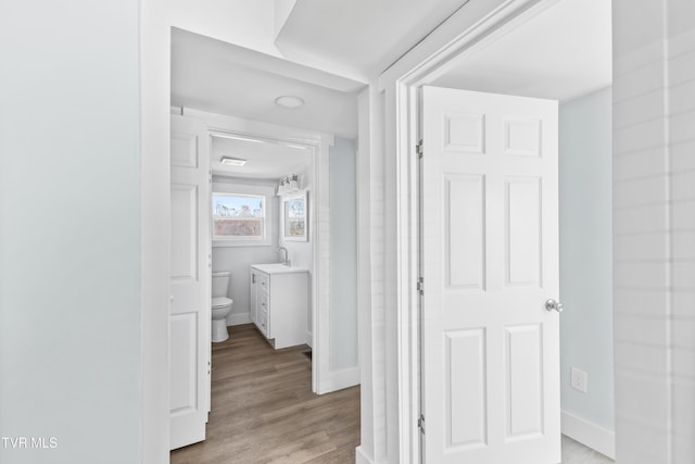 hallway featuring light wood finished floors, a sink, and baseboards