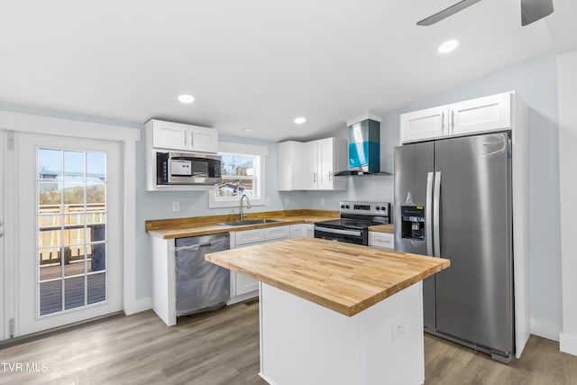 kitchen featuring appliances with stainless steel finishes, butcher block counters, a sink, and wall chimney range hood