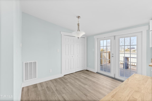 unfurnished dining area with light wood-type flooring, baseboards, visible vents, and vaulted ceiling