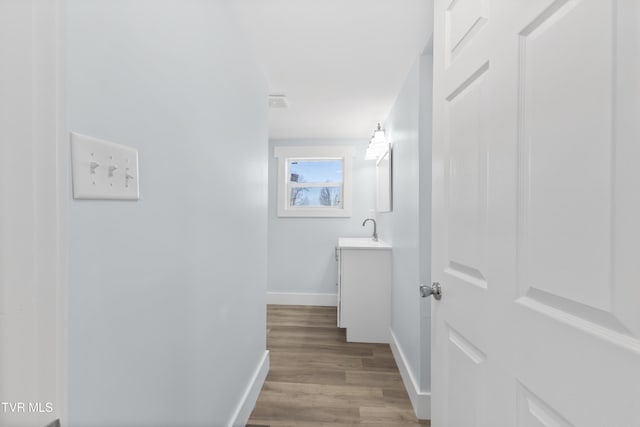 hallway featuring visible vents, a sink, baseboards, and wood finished floors