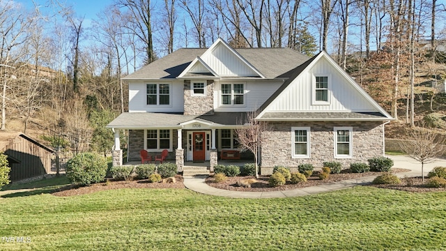 craftsman-style house featuring covered porch, a shingled roof, stone siding, a front lawn, and board and batten siding