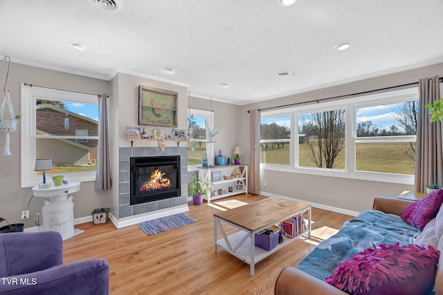 living room with ornamental molding, a textured ceiling, a tiled fireplace, and wood finished floors