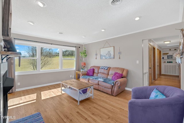 living room featuring visible vents, baseboards, light wood-style flooring, ornamental molding, and a textured ceiling