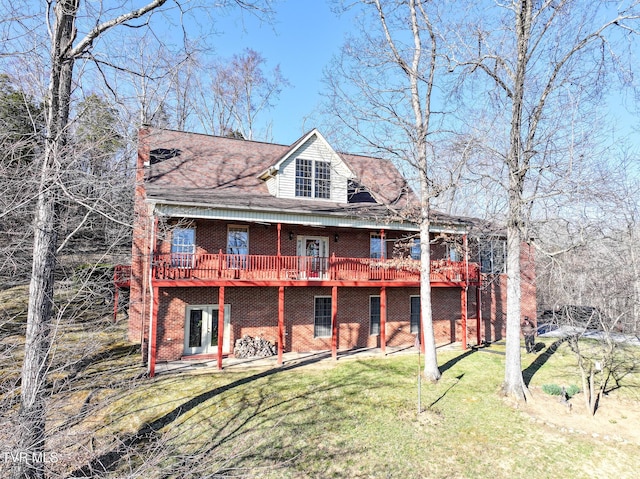 back of house featuring a deck, brick siding, a yard, french doors, and a chimney