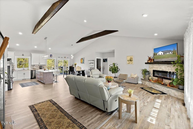 living area with a fireplace, recessed lighting, light wood-style flooring, high vaulted ceiling, and beamed ceiling