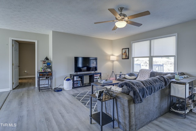 living area featuring a textured ceiling, ceiling fan, wood finished floors, and baseboards