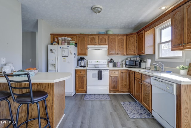 kitchen featuring white appliances, a breakfast bar, wood finished floors, under cabinet range hood, and a sink